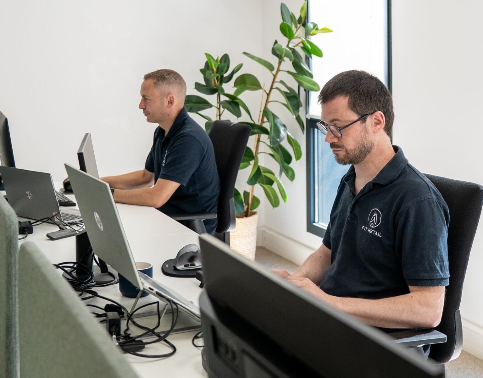 Collaborateur Fit Retail au bureau, double écran et plante verte