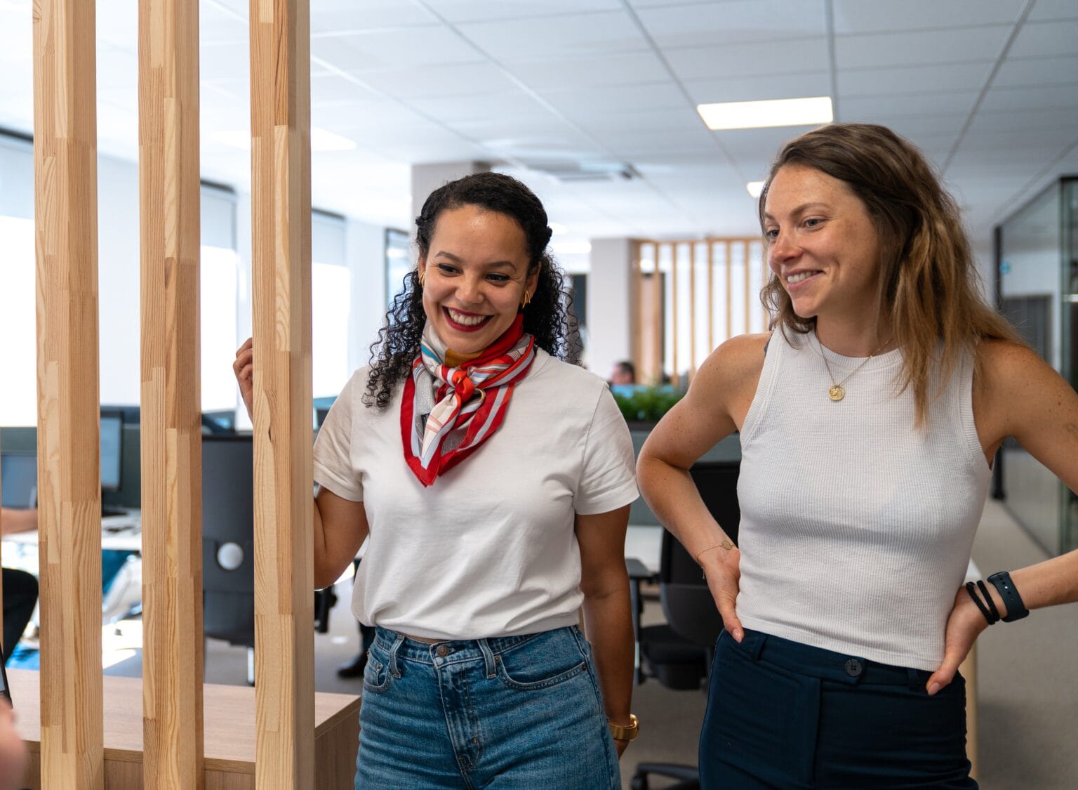 Deux collègues Fit Retail discutant avec le sourire près d'une cloison en bois