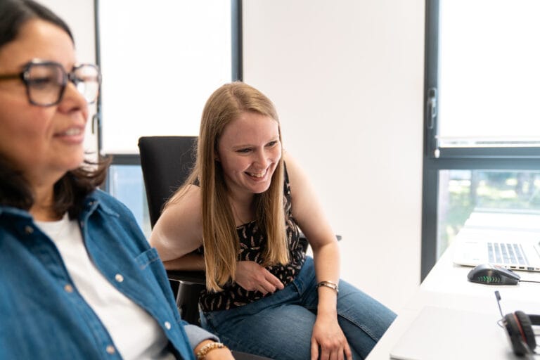 Collaboratrice Fit Retail souriante en train de discuter avec sa voisine de bureau