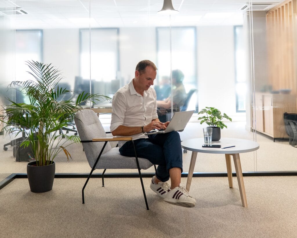 Collaborateur Fit Retail au bureau dans un espace lumineux avec plante verte en train de travailler avec son ordinateur sur les genoux